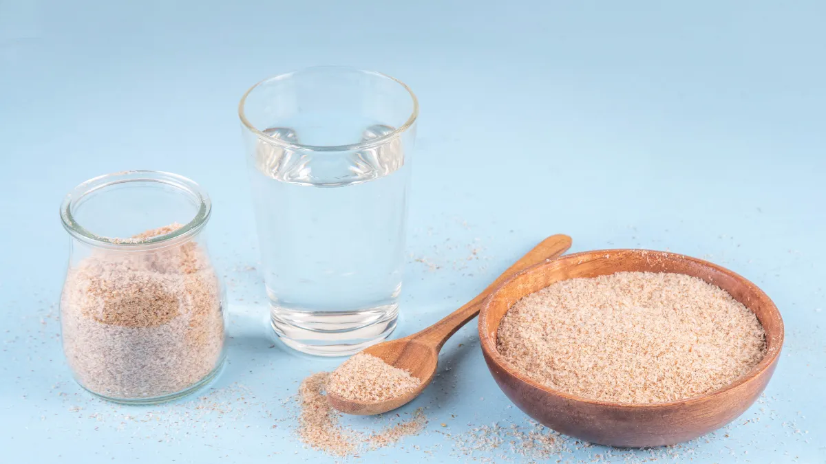 Psyllium husk powder in a wooden bowl and glass jar alongside a glass of water