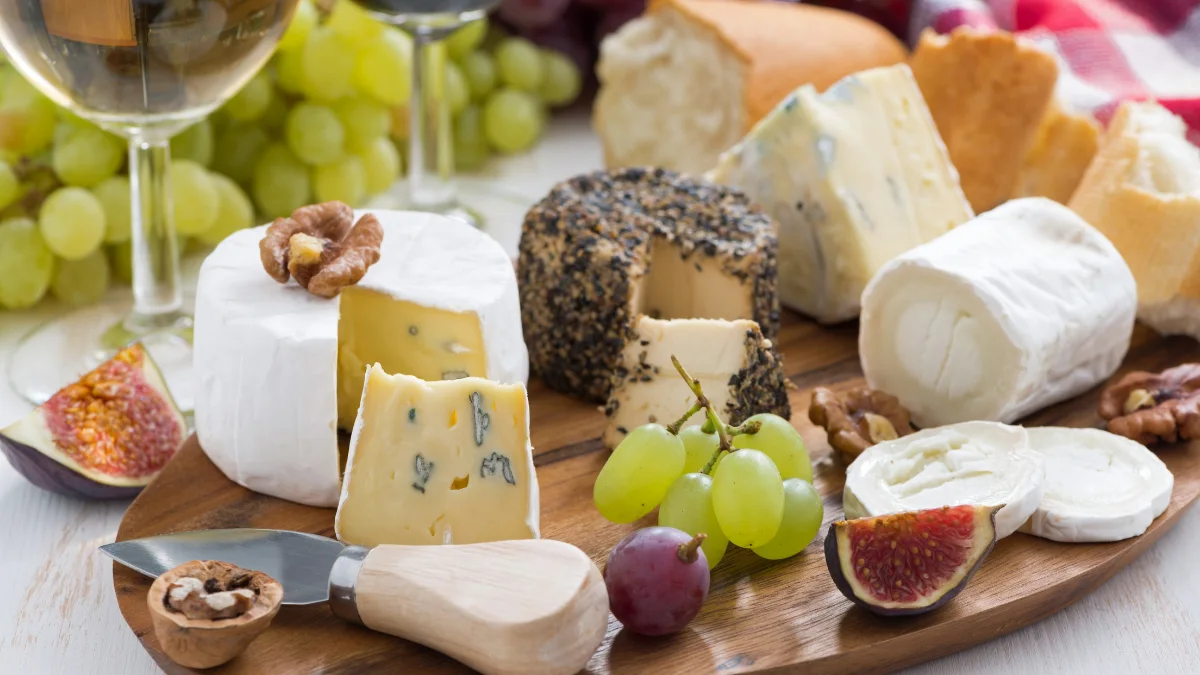 A cheese board with a variety of cheeses, grapes, figs, walnuts and a glass of wine